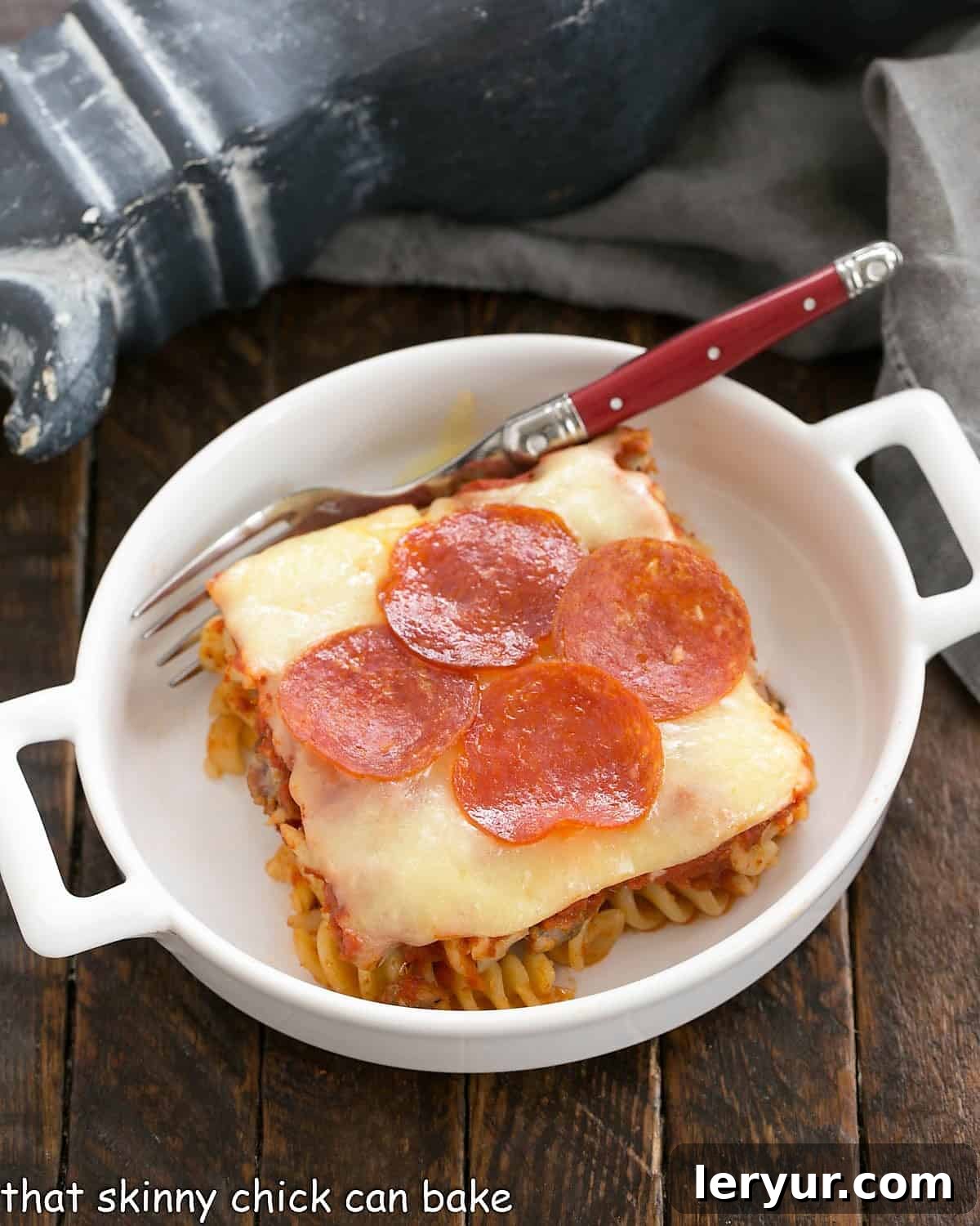 Effortless Pizza Delight 2 Overhead view of one sliced of pizza casserole in a white dish with a red handle fork.