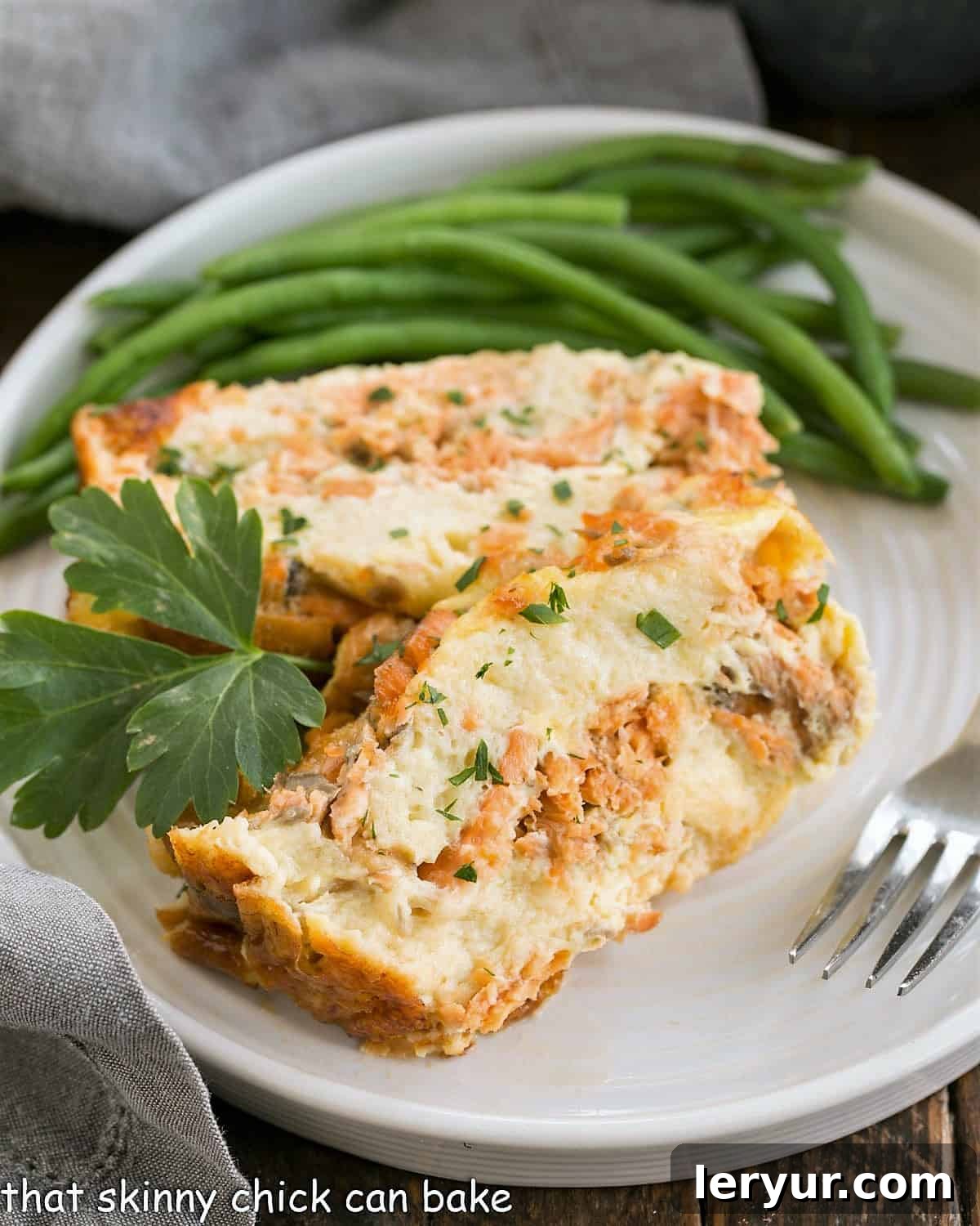 Two generous slices of golden-brown baked salmon loaf are served on a round white plate, accompanied by vibrant green beans, suggesting a complete and wholesome meal.