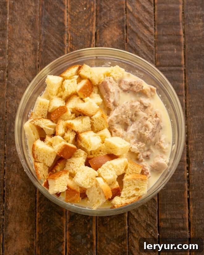 Cubed brioche bread and flaked canned salmon are gently tossed into a creamy egg and milk mixture in a large mixing bowl.