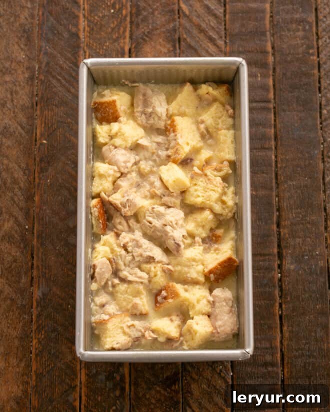 The salmon loaf mixture is being carefully spooned and spread into a prepared loaf pan, ensuring an even layer.
