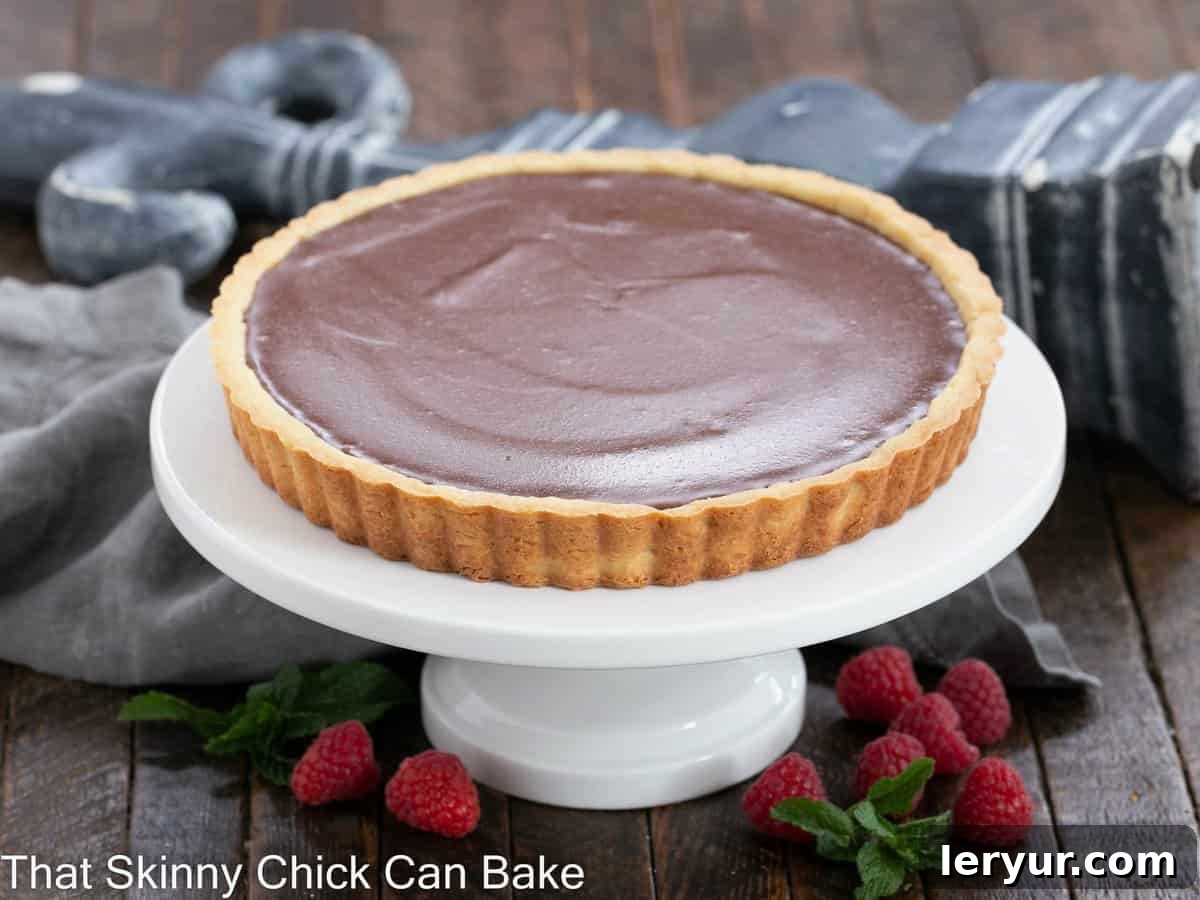 A whole milk chocolate tart, exquisitely presented on a pristine white cake stand, ready for serving.