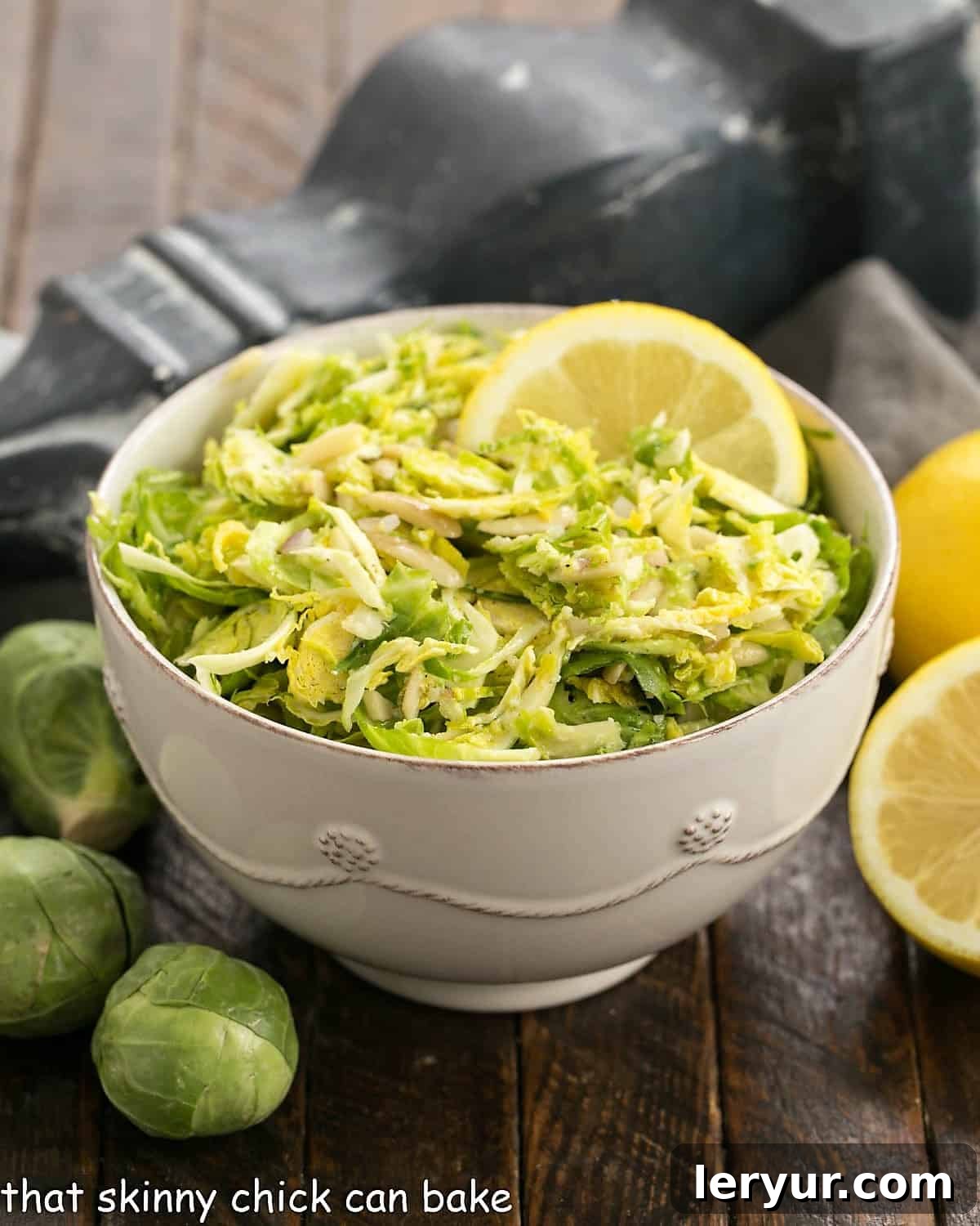 Brussels Sprouts Slaw with Lemon Vinaigrette 3 Side view of a bowl of Brussels sprouts salad in a white ceramic bowl, garnished with lemon.