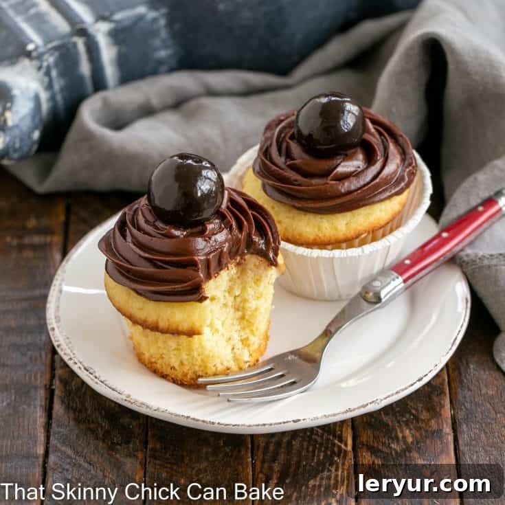 Two beautifully frosted yellow cupcakes on a white dessert plate, highlighting the rich ganache.