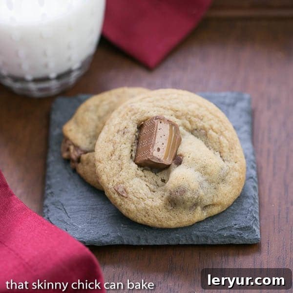 Two freshly baked Milky Way Cookies resting on a grey stone coaster atop a rustic wooden table.