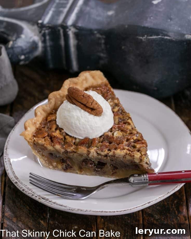 Slice of derby pie on a dessert plate topped with whipped cream and a pecan
