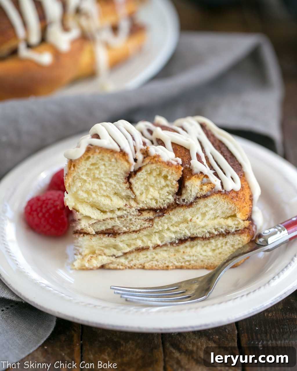 A beautifully baked slice of Cinnamon Twist Bread resting on a white plate, ready to be enjoyed with a red-handled fork.