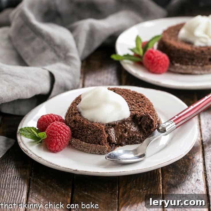Two perfectly baked lava cakes on white dessert plates, elegantly garnished with a generous swirl of Kahlua whipped cream, vibrant fresh berries, and delicate mint leaves, highlighting their appealing presentation.