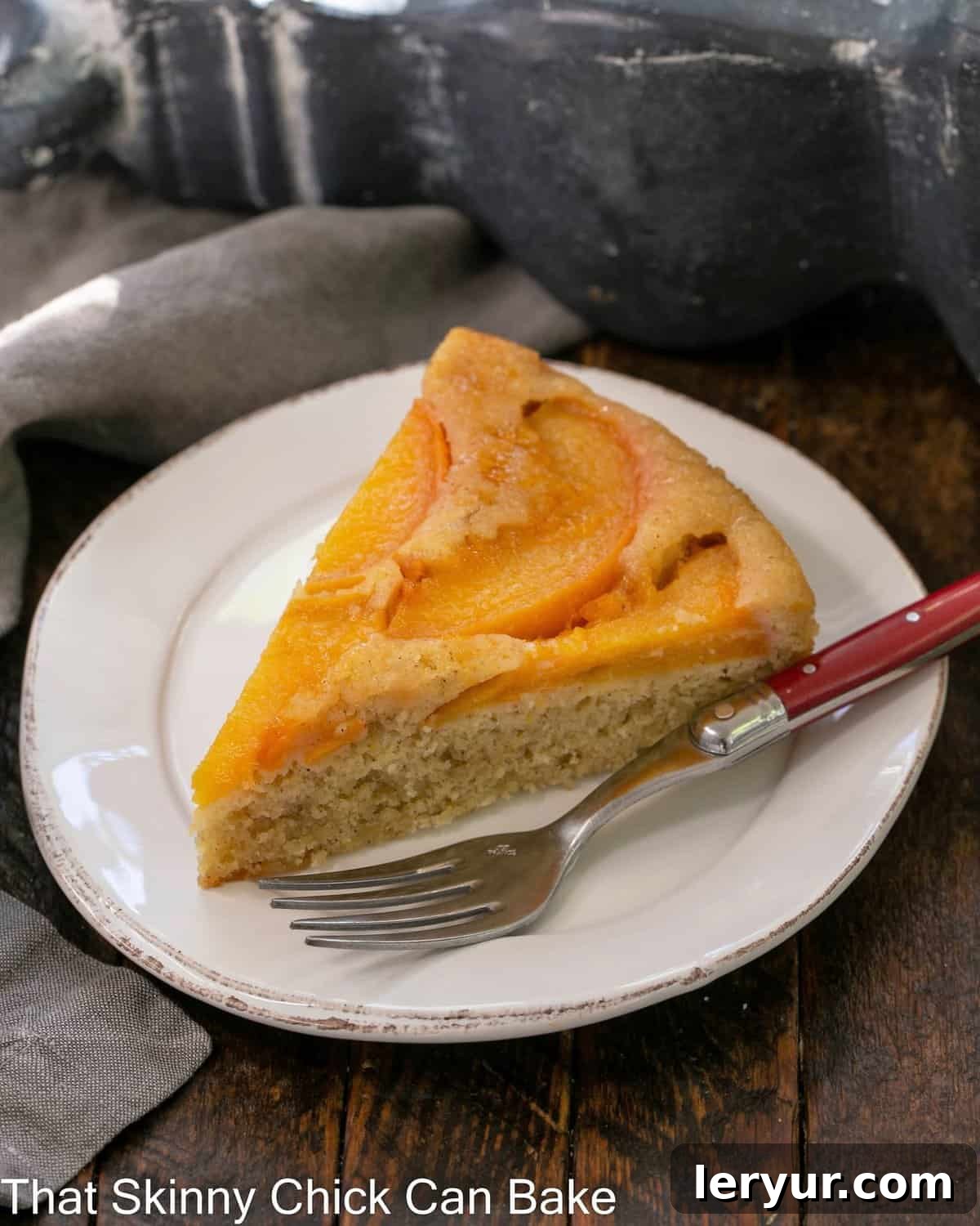 Caramelized Peach Flip Cake 2 A slice of peach upside down cake on a white dessert plate with a red handle fork, showing the beautiful caramelized peach topping.