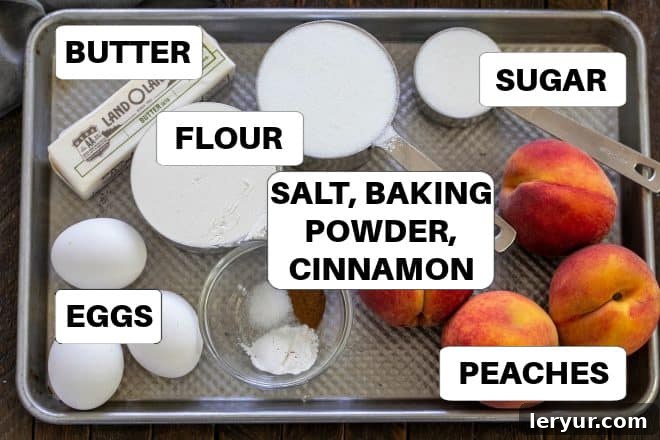 Caramelized Peach Flip Cake 3 Peach Upside Down Cake Ingredients with labels on a sheetpan, showcasing fresh peaches, butter, sugar, flour, and eggs.