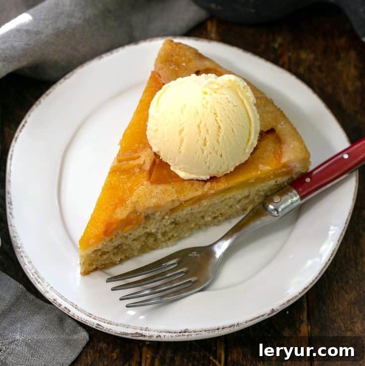 Overhead view of a slice of peach upsidedown cake with a scoop of vanilla ice cream on a white plate with a red handled fork, highlighting the luscious peaches.