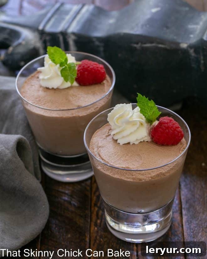 2 dishes of chocolate mousse garnished with whipped cream, raspberries and mint