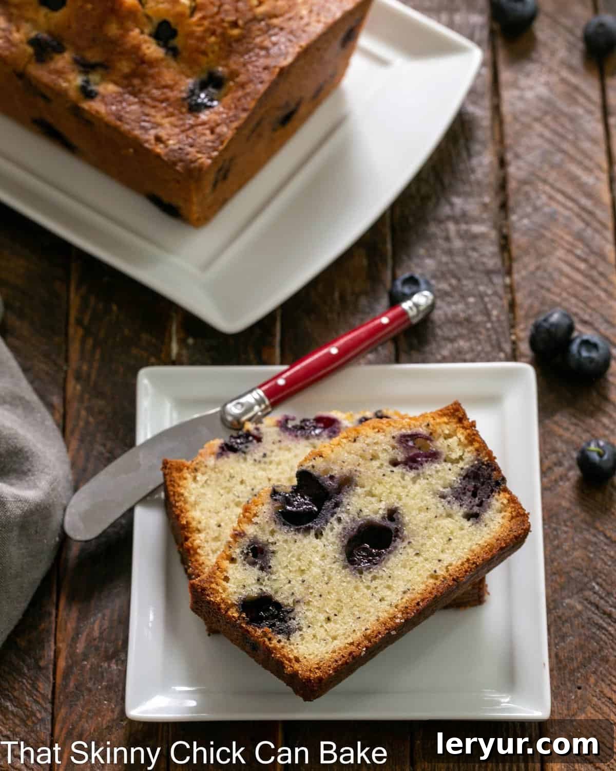 Morning Blueberry Poppy Seed Bake 3 Two slices of moist blueberry poppy seed bread on a white plate in front of a full loaf on a serving tray, ready to be enjoyed.