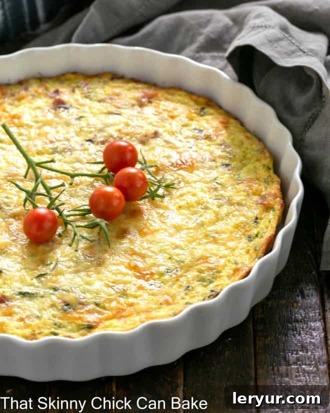 Savory Zucchini and Prosciutto Quiche 3 Crustless Zucchini Quiche in a shallow white souffle dish with a fresh cherry tomato garnish, highlighting its appealing presentation.