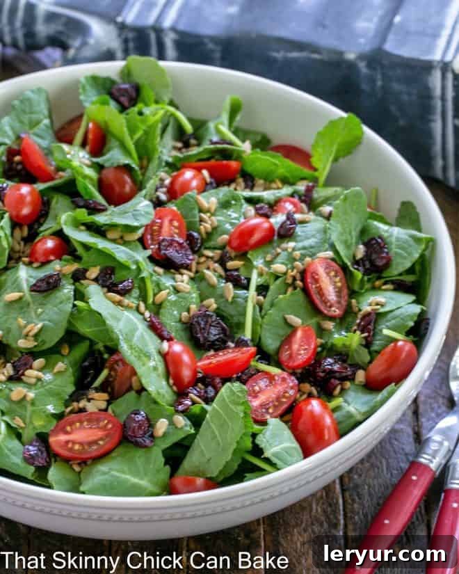 Kale salad with cranberries, tomatoes and sunflower seeds in a large white serving bowl.