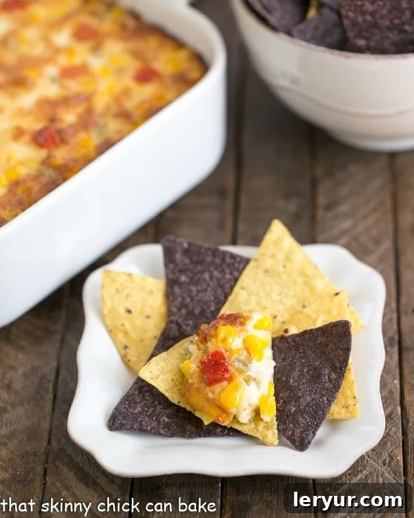 A vibrant close-up of Fiesta Corn Dip served on a tortilla chip, highlighting the melted cheese and corn kernels, presented on a clean white background.