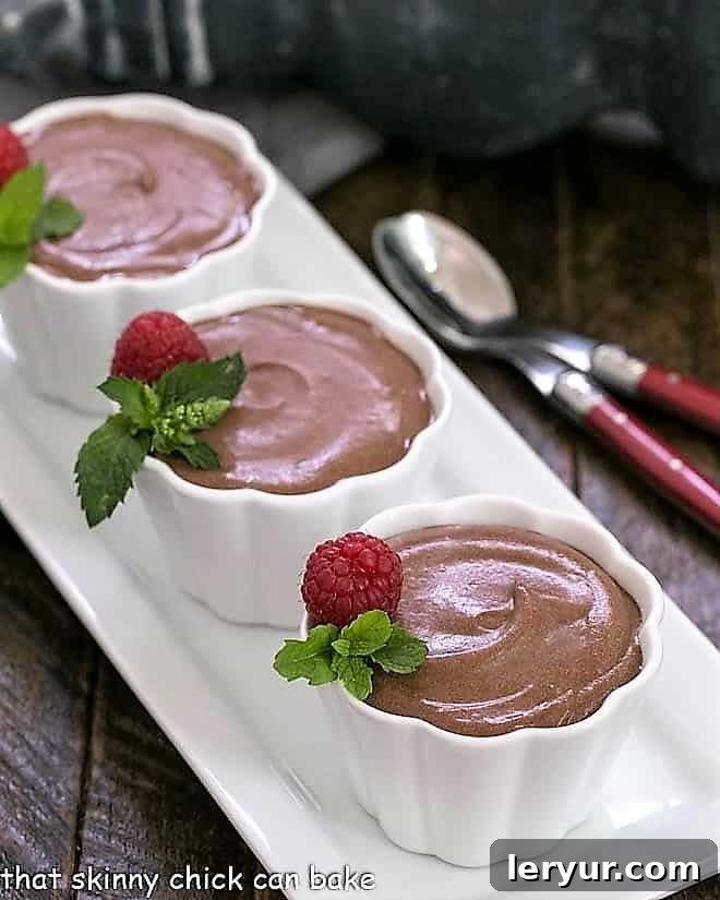 Julia Child's Mousseline au Chocolat - a classic French recipe to make a rich, luscious chocolate mousse Mousseline au chocolate in white ramekins on a white tray, garnished with fresh raspberries and a sprig of mint.