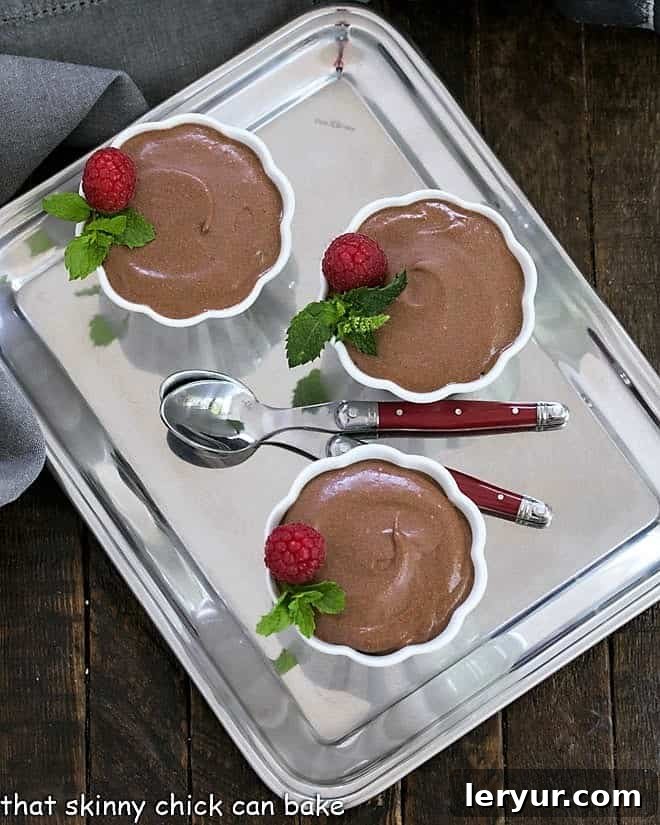 How to Make Chocolate Mousse - a classic French recipe to make a rich, luscious chocolate mousse 3 cups of chocolate mousse on a silver tray with two spoons, garnished with chocolate shavings and mint.