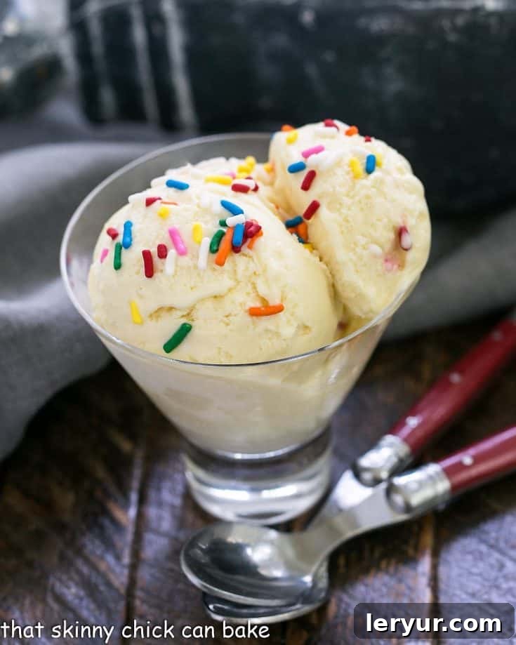 Two scoops of cake batter ice cream in a glass dish with two red-handled spoons, showcasing its vibrant color and creamy texture.