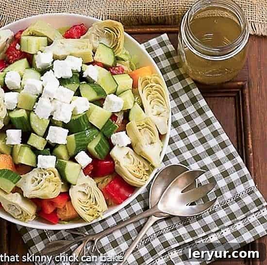 A beautifully presented Greek Salad with Feta in a white serving bowl, accompanied by salad serving utensils and a jar of homemade vinaigrette, highlighting its freshness and vibrant colors.