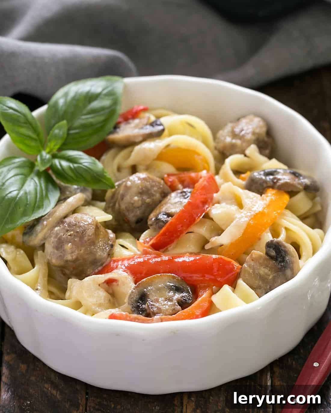 Sausage, Pepper, Mushroom Fettuccine - a twist on the classic Fettuccine Alfredo with the addition of bell peppers, mushrooms and sausage A bowl of Sausage, Pepper, Mushroom Fettuccine, a creamy pasta dish with a red-handled fork.
