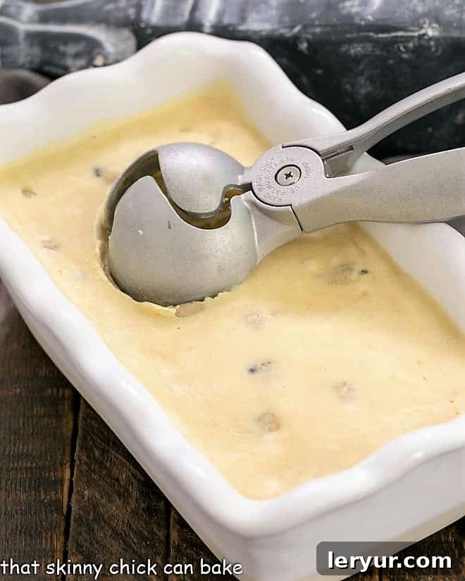 Cookie dough ice cream frozen in a white loaf pan with an ice cream scoop.