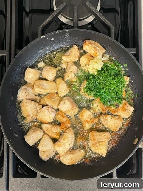 Zesty Garlic Parsley Chicken 5 Adding minced garlic, fresh parsley, and butter to the cooked chicken in a skillet.
