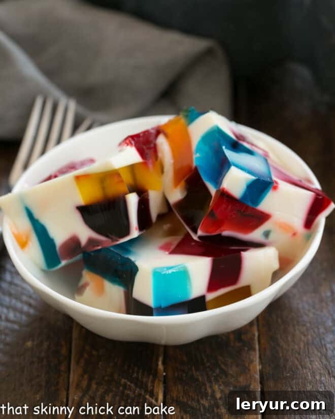 A small white dish filled with colorful Broken Glass Jello squares, ready to be served, showcasing the intricate stained-glass effect.