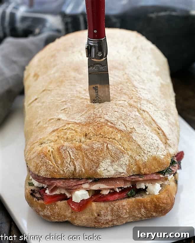 The Pressed Picnic Loaf 2 A large Italian Picnic Sandwich, beautifully arranged on a ceramic tray before slicing, showing off its generous fillings within the ciabatta bread.