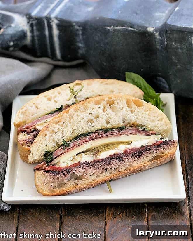 Italian Picnic Sandwich - a pressed brick sandwich filled with meat, cheese, vegetables and olive paste. Perfect for sharing with family and friends Delightful slices of an Italian Picnic Sandwich, featuring layers of meat, cheese, and vegetables, beautifully arranged on a white plate, ready for sharing.