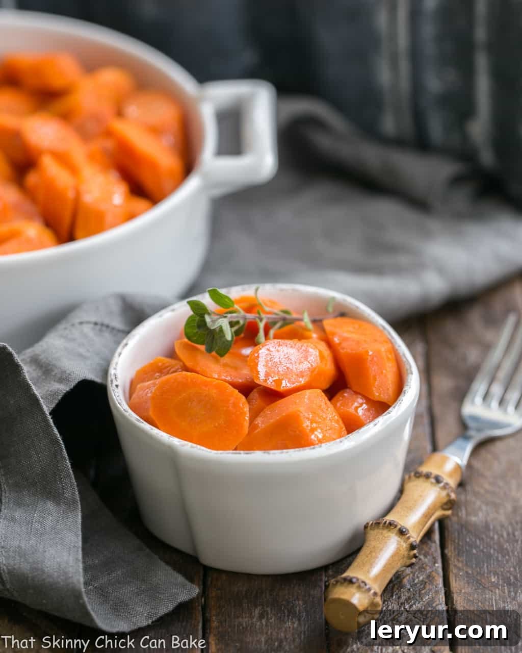 Bourbon Maple Glazed Carrots - An easy way to transform carrots into a restaurant worthy side dish! A small white bowl filled with Bourbon Maple Glazed Carrots, garnished with fresh herbs, and a bamboo fork resting beside it.
