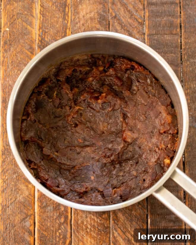 A saucepan on the stove containing a rich, dark date filling, gently simmering.