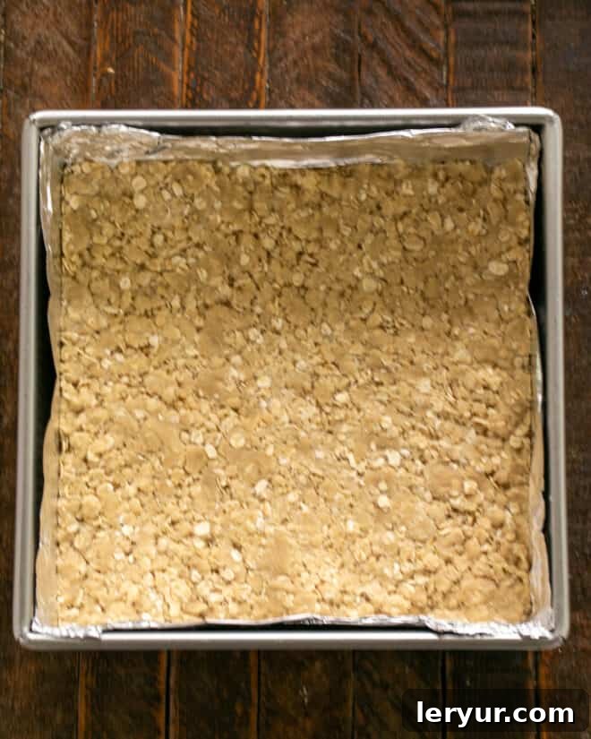 Half of the streusel crumb mixture evenly pressed into the bottom of a square baking pan, forming the crust.