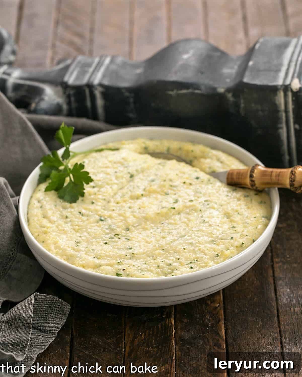 Easy Parmesan Polenta in a white bowl with a bamboo handle spoon garnished with fresh parsley.