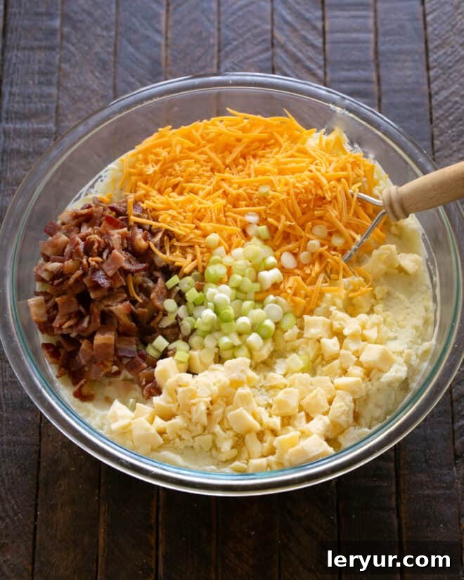Cooked bacon, cubed and grated cheddar cheeses, and sliced green onions being added to the mashed potato mixture.