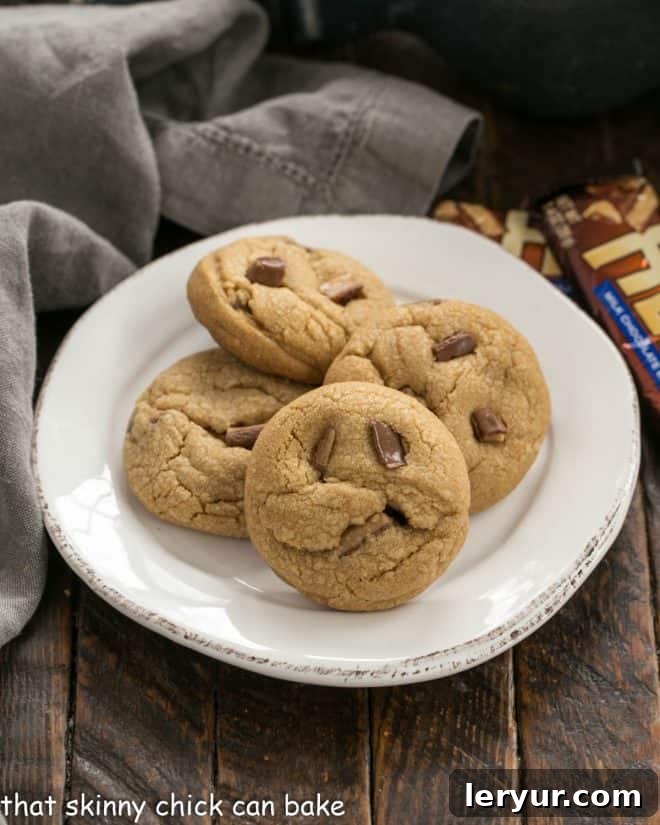 Four golden-brown Toffee Biscoff Cookies artfully arranged on a clean white plate, showcasing their delightful texture and inviting appearance.