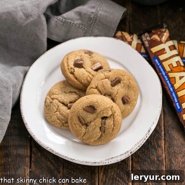Overhead view of several golden-brown Biscoff Toffee Cookies on a white plate next to two Heath bars, highlighting the key ingredients.