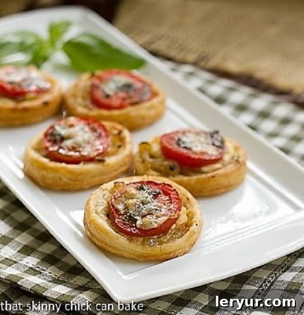Tomato and Boursin Tartlets lined up on a white ceramic tray with a sprig of basil, ready for serving.