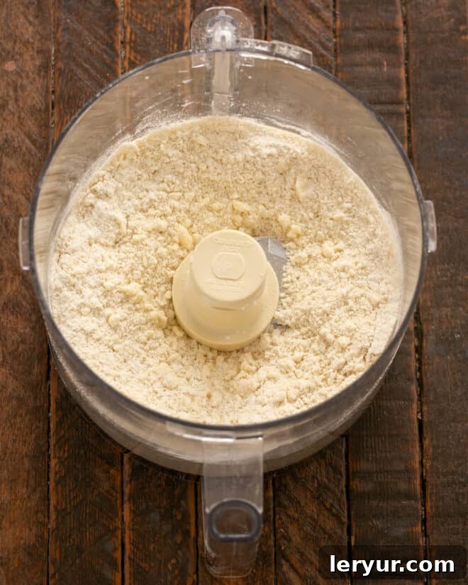 Food processor contents resembling coarse cornmeal with pea-sized fat chunks.