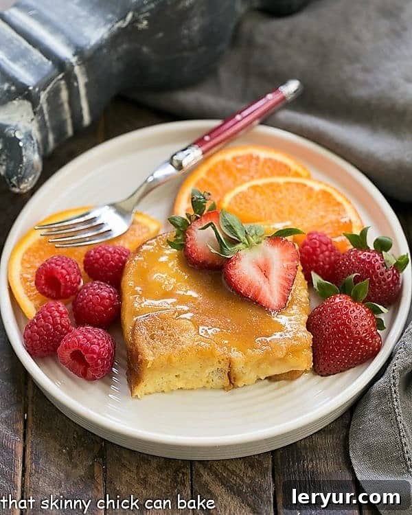 Creme Brulee French Toast - an exquisite, make ahead breakfast casserole! Crème Brûlée French Toast on a round plate with fresh berries and a red handled fork, highlighting its rich, caramelized top and soft interior.