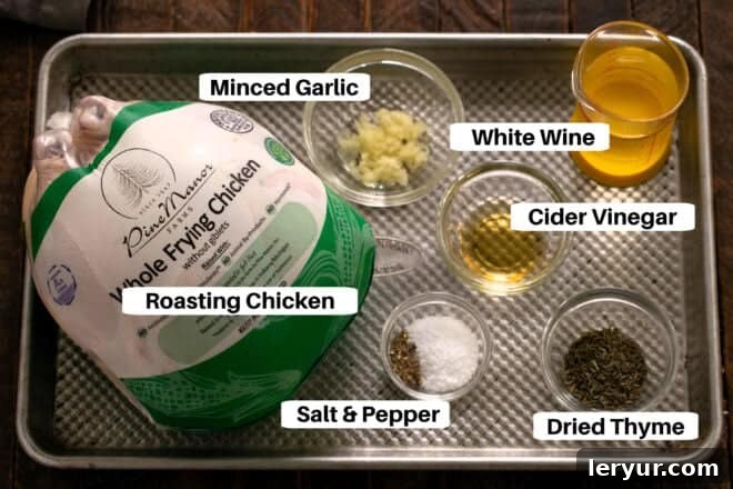 Golden Crispy Roasted Chicken 2 A curated display of raw ingredients for Oven Roasted Chicken, including a whole chicken, fresh garlic, dried thyme, cider vinegar, and white wine, neatly arranged on a metal sheet pan.