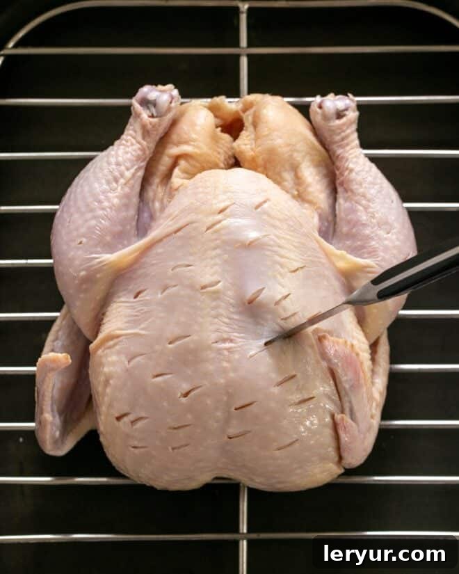 Golden Crispy Roasted Chicken 3 A close-up image showing a whole raw chicken being prepared with the slashing technique, demonstrating the precise cuts being made into the meat.
