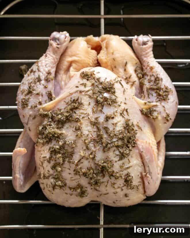 Golden Crispy Roasted Chicken 5 A whole chicken generously coated with the garlic and thyme seasoning mixture, showing the rub worked into the slashes, placed on a roasting pan.