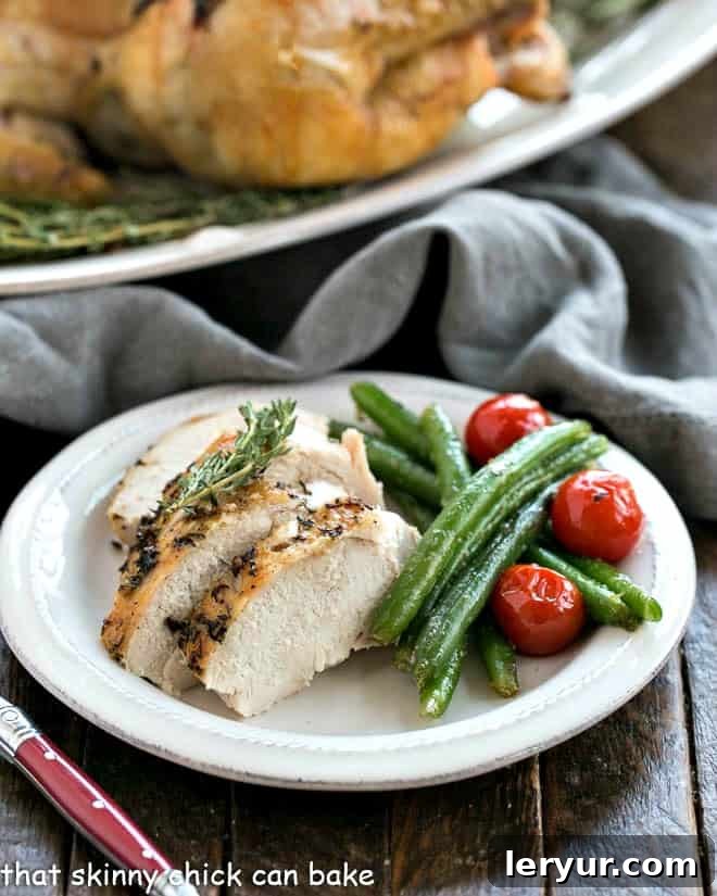 Oven Roasted Chicken- A slashing technique and a few ingredients make for a succulent entree! A whole roasted chicken, expertly sliced to reveal its juicy interior, served on a pristine white plate alongside fresh green beans, highlighting its readiness to be enjoyed.