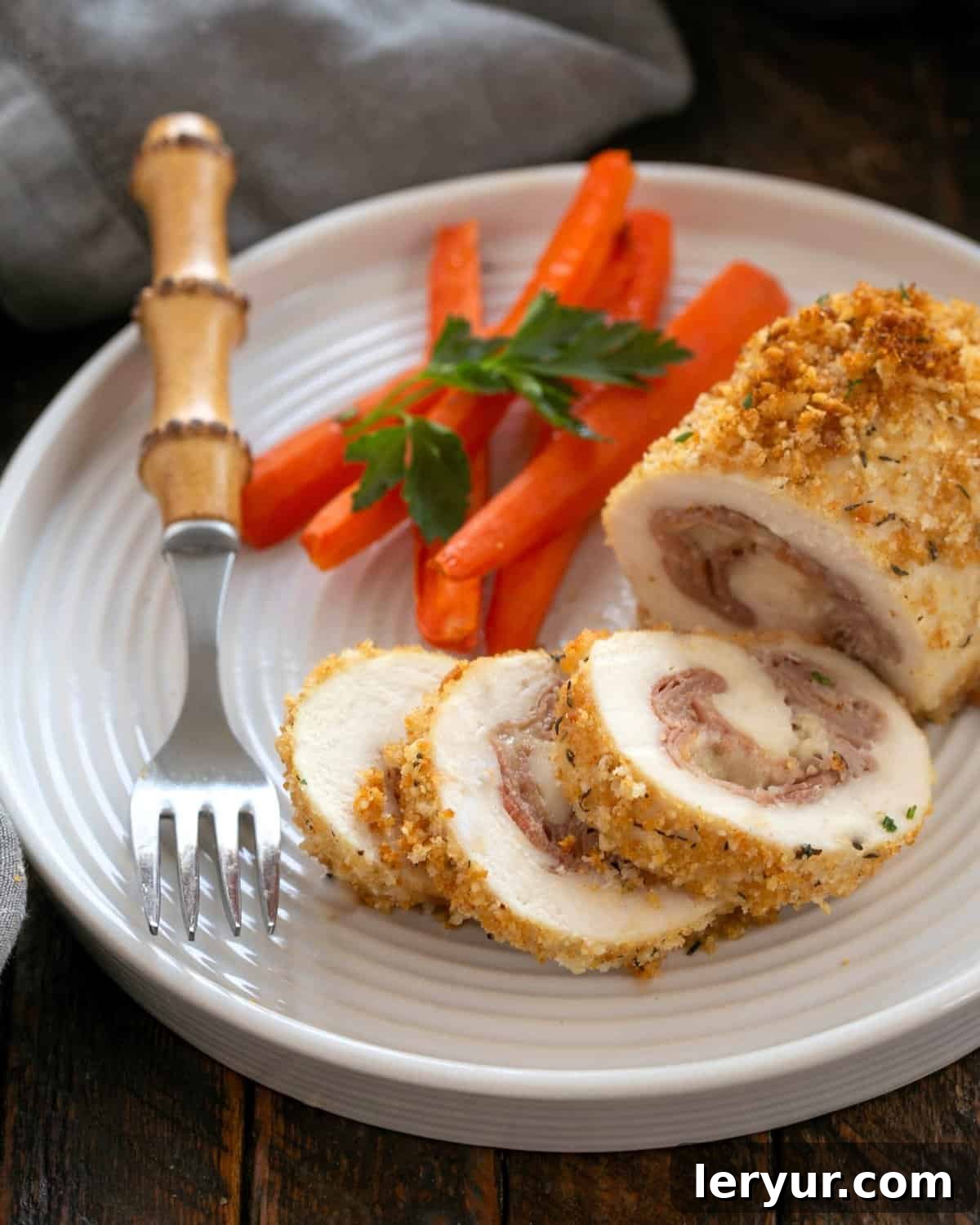 Chicken Cordon Bleu partially sliced on a white plate with carrots and a fork.