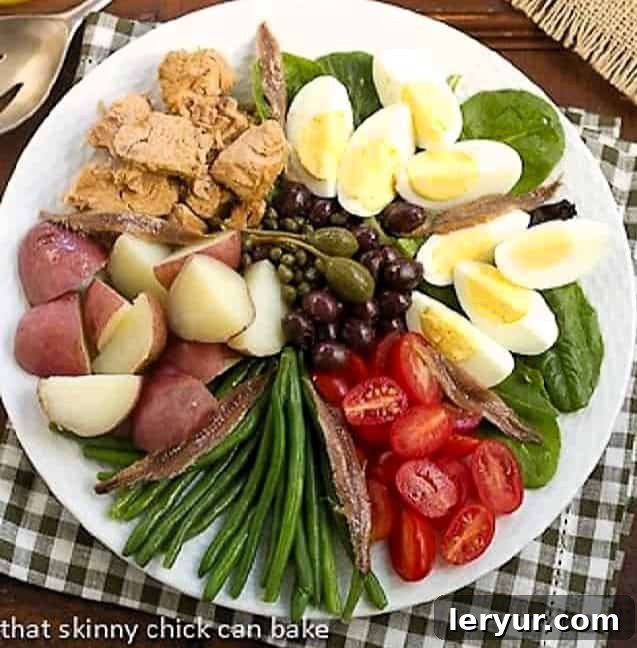 Classic French Salade Niçoise - Dorie Greenspan's delicious version of this classic French salad! A beautifully arranged Classic French Salade Niçoise on a white plate, showcasing fresh ingredients like tuna, green beans, potatoes, and eggs.