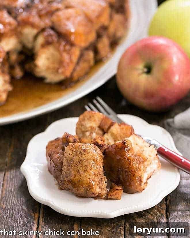 A close-up of a serving of Apple Monkey Bread on a white ceramic plate with a red handled fork, highlighting the sticky apple pieces.