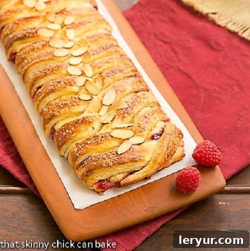 A freshly baked Raspberry Danish Braid resting on a rustic wooden cutting board, showcasing its golden crust and intricate braid pattern, ready to be sliced and served.