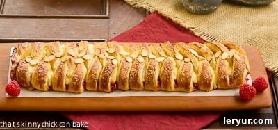 Close-up horizontal view of a Raspberry Danish Braid on a cutting board, illustrating the distinct cuts made along the sides of the filling before braiding.