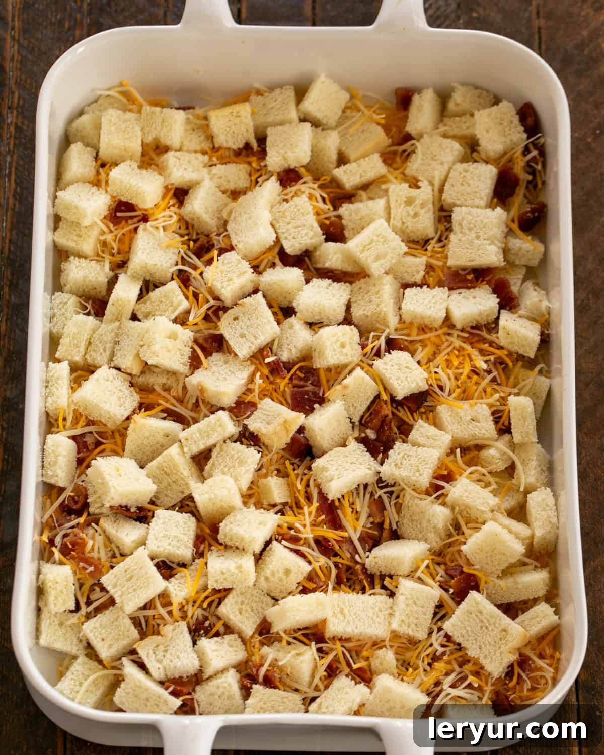 Bread cubes, bacon and cheese in the baking dish, ready for the egg mixture.