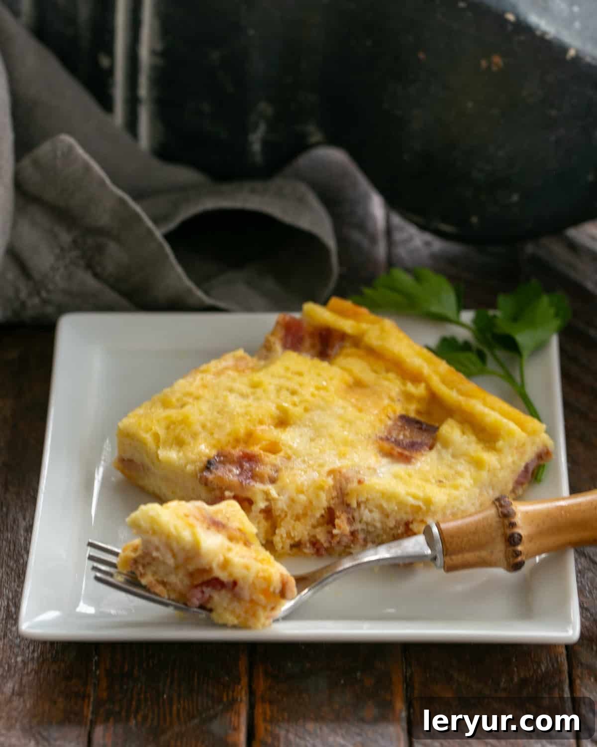 A perfectly cooked slice of bacon and egg casserole on a white plate with a fork.